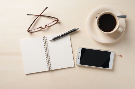 Opened notebook with blank area, pen, smart phone, and coffee cup on wood table in morning time