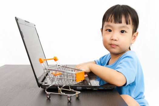 Chinese little girl using laptop with small shopping cart in plain isolated white background.