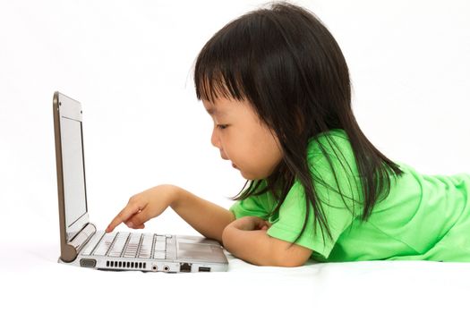 Chinese little girl lying down with laptop in plain white isolated background.