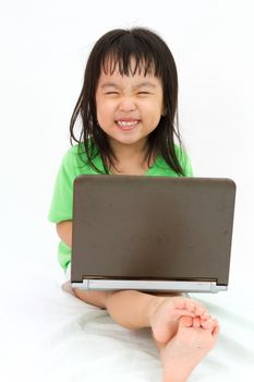 Chinese little girl sitting on floor with laptop in plain isolated white background.
