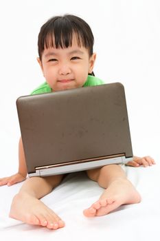 Chinese little girl sitting on floor with laptop in plain isolated white background.