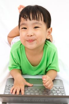 Chinese little girl lying down with laptop in plain white isolated background.