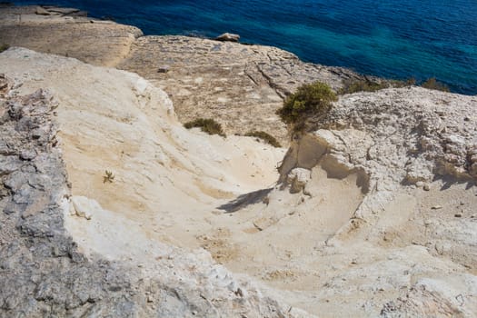 Sand color of the rocks. Coast of mediterranean island Malta, city Marsaskala. Blue water of the sea.