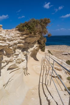 Sand color of the rocks. Coast of mediterranean island Malta, city Marsaskala. Horizon of a blue water. Bright blue sky with some clouds.