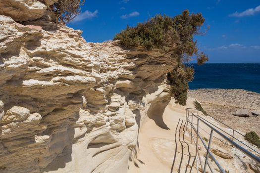 Sand color of the rocks. Coast of mediterranean island Malta, city Marsaskala. Horizon of a blue water. Bright blue sky with some clouds.