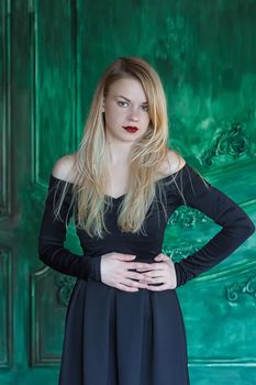 Elegant blonde in a black dress near grunge wall green