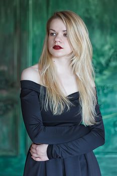 Elegant blonde in a black dress near grunge wall green