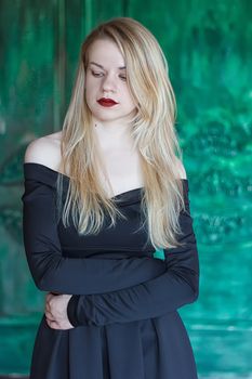 Elegant blonde in a black dress near grunge wall green