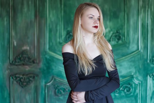 Elegant blonde in a black dress near grunge wall green