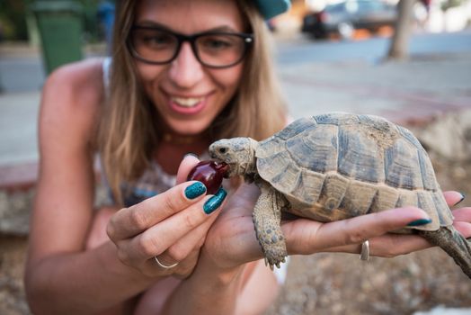 Happy young woman feeding turtle with cherry