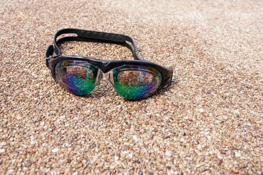 Glasses for swimming on a cement floor with small stone near swimming pool.