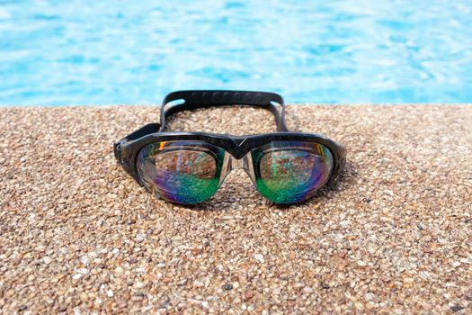 Glasses for swimming on a cement floor with small stone near swimming pool.