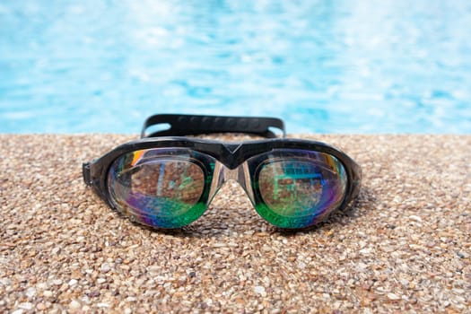 Glasses for swimming on a cement floor with small stone near swimming pool.