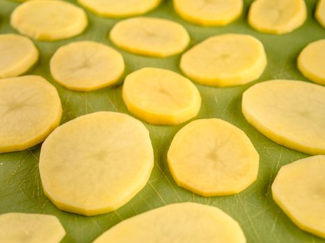 Pattern of sliced peeled potatoes on green used plastic board, simple food preparation illustration, vegetarian dieting, still life with center composition, close up