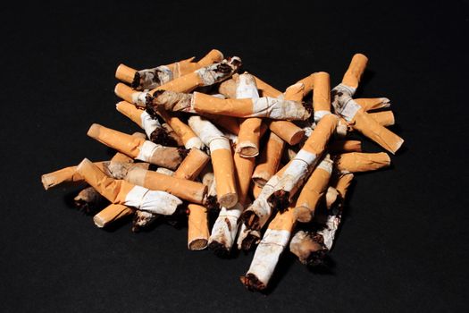 Pile of used cigarette butts on black background