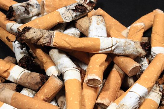 Closeup on pile of used cigarette butts on black background
