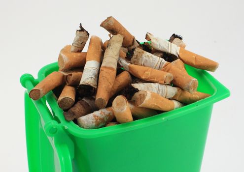 Used cigarette butts in green waste bin on white background