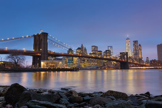 Brooklyn bridge and New York City Manhattan downtown skyline at dusk with skyscrapers illuminated over East River panorama. 