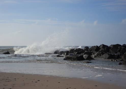 Beach at ocean with breaking waves and black rocks