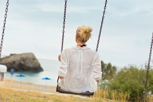 Young blonde woman sitting on the swing on beach.