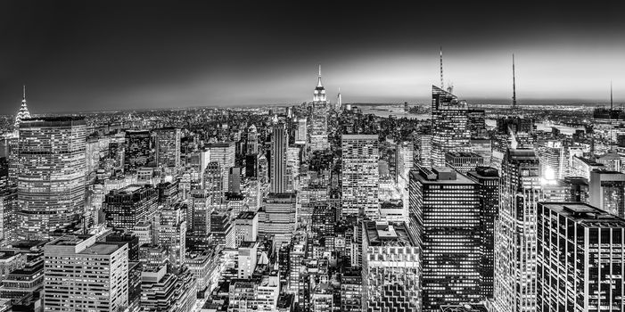 New York City. Manhattan downtown skyline with illuminated Empire State Building and skyscrapers at dusk. Black and white image. Panoramic composition.