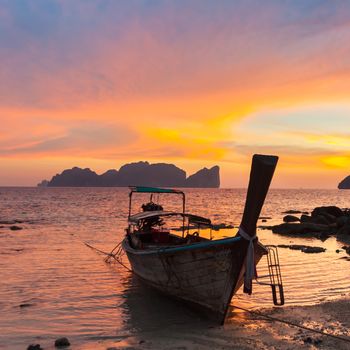 Traditional thai wooden longtail boat on beach of Phi-Phi Don island in sunset. Silhouette of famous Phi Phi Lee island in background. Thailand, Krabi province.