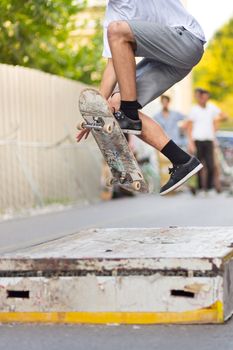 Young skateboarder skateboarding on an object in street. Skateboarding legs doing trick ollie at skate park. Group of friends cheering in the background.