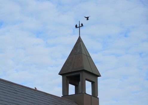 Bell tower of small simple church with cross and birds