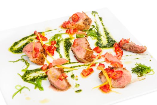 veal meat medallions with pesto sauce, vegetables and seaweed on white plate