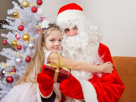 Little girl hugging Santa Claus which is holding a gift