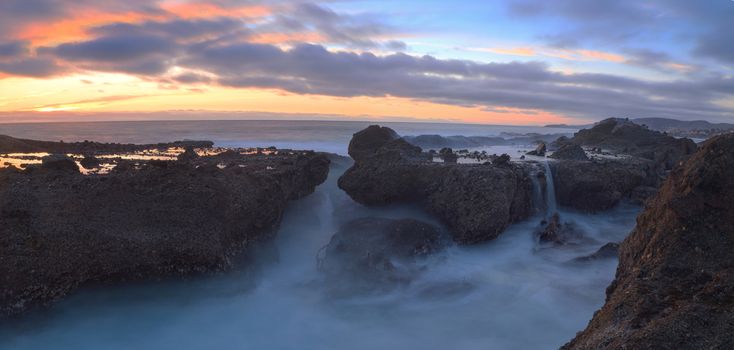 Long exposure of sunset over rocks, giving a mist like effect over ocean in Laguna Beach, California, United States