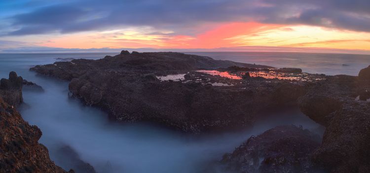 Long exposure of sunset over rocks, giving a mist like effect over ocean in Laguna Beach, California, United States