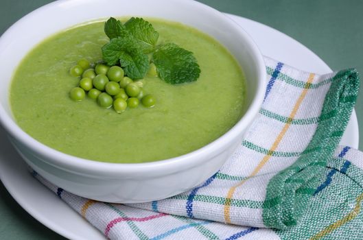 A plate of soup puree of green peas with mint on a table