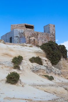 Sand color of the rocks with curved shape and an old building. Coast of island Malta, city Marsaskala. Blue sky with several white clouds.