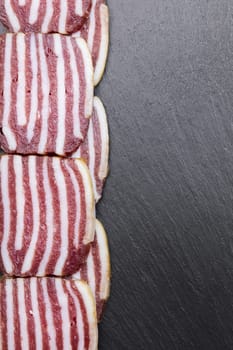 slices of sausage with bacon on dark background