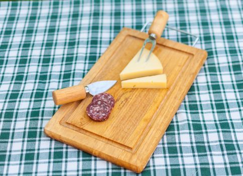 Sausage and cheese on a wooden chopping board outside in summer