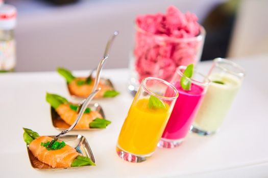 Appetizer plate of sauteed asparagus wrapped in thin slices of smoked salmon and different vegetable juice . Closeup with selective focus and shallow depth of field.
