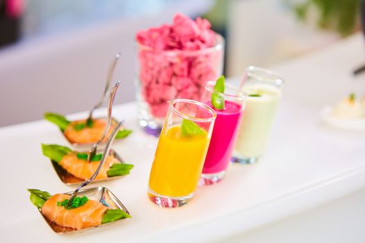 Appetizer plate of sauteed asparagus wrapped in thin slices of smoked salmon and different vegetable juice . Closeup with selective focus and shallow depth of field.