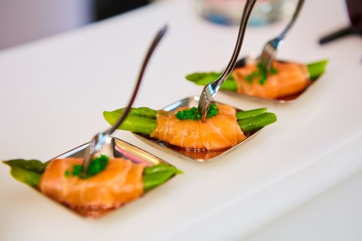 Appetizer plate of sauteed asparagus wrapped in thin slices of smoked salmon and different vegetable juice . Closeup with selective focus and shallow depth of field.