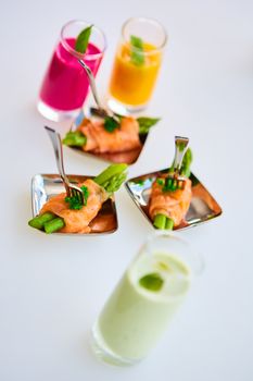 Appetizer plate of sauteed asparagus wrapped in thin slices of smoked salmon and different vegetable juice . Closeup with selective focus and shallow depth of field.