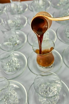 Pouring turkish coffee into traditional embossed glass cup.
