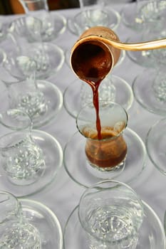 Pouring turkish coffee into traditional embossed glass cup.