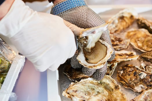 Fresh oyster held open with a oyster knife in a hand with an oyster glove