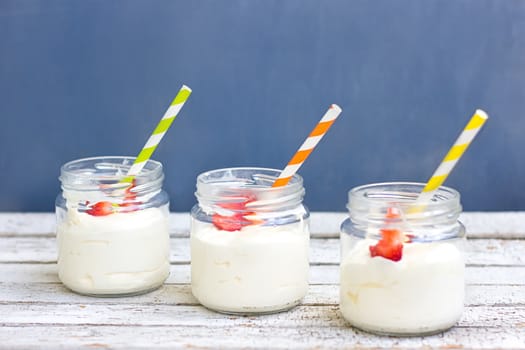 Three in a jar of yogurt with strawberries on a wooden board on a blue background