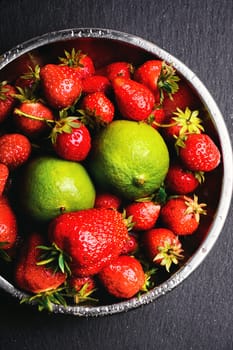 iron plate with ripe strawberry fruit and lime on a dark background