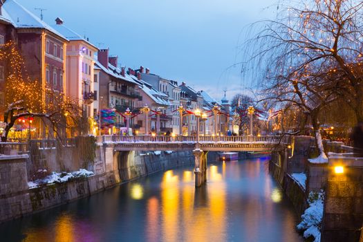 View of lively river Ljubljanica bank with Cobblers' Bridge in old city center decorated with Christmas lights. Ljubljana, Slovenia, Europe. Shot at dusk.