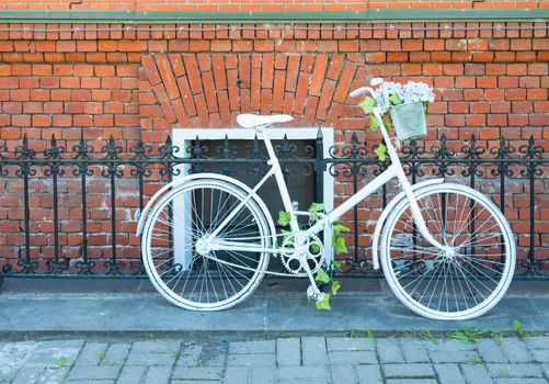 White painted bike stands by metal fence in front of a brick wall