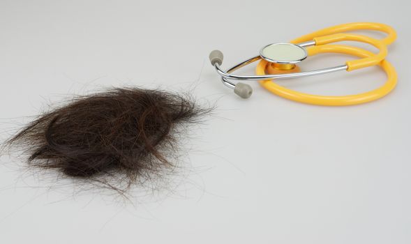 Group of brown lost hair and yellow stethoscope on white background.