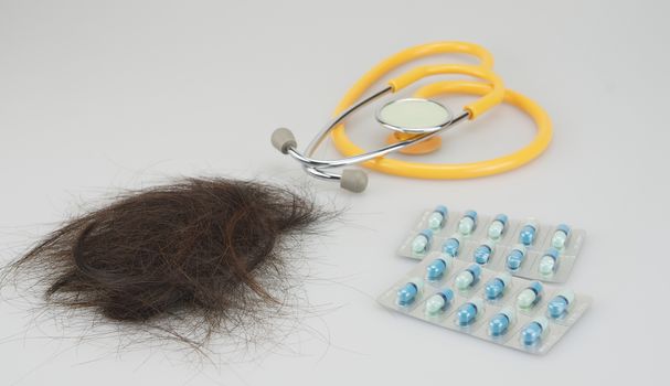 Brown lost hair with stethoscope and medicine placed on white background.