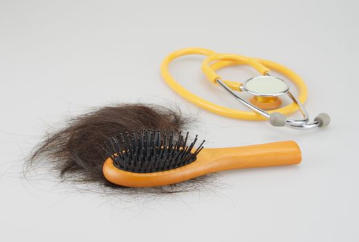 Wooden hair brush with lost brown hair and stethoscope on white background.